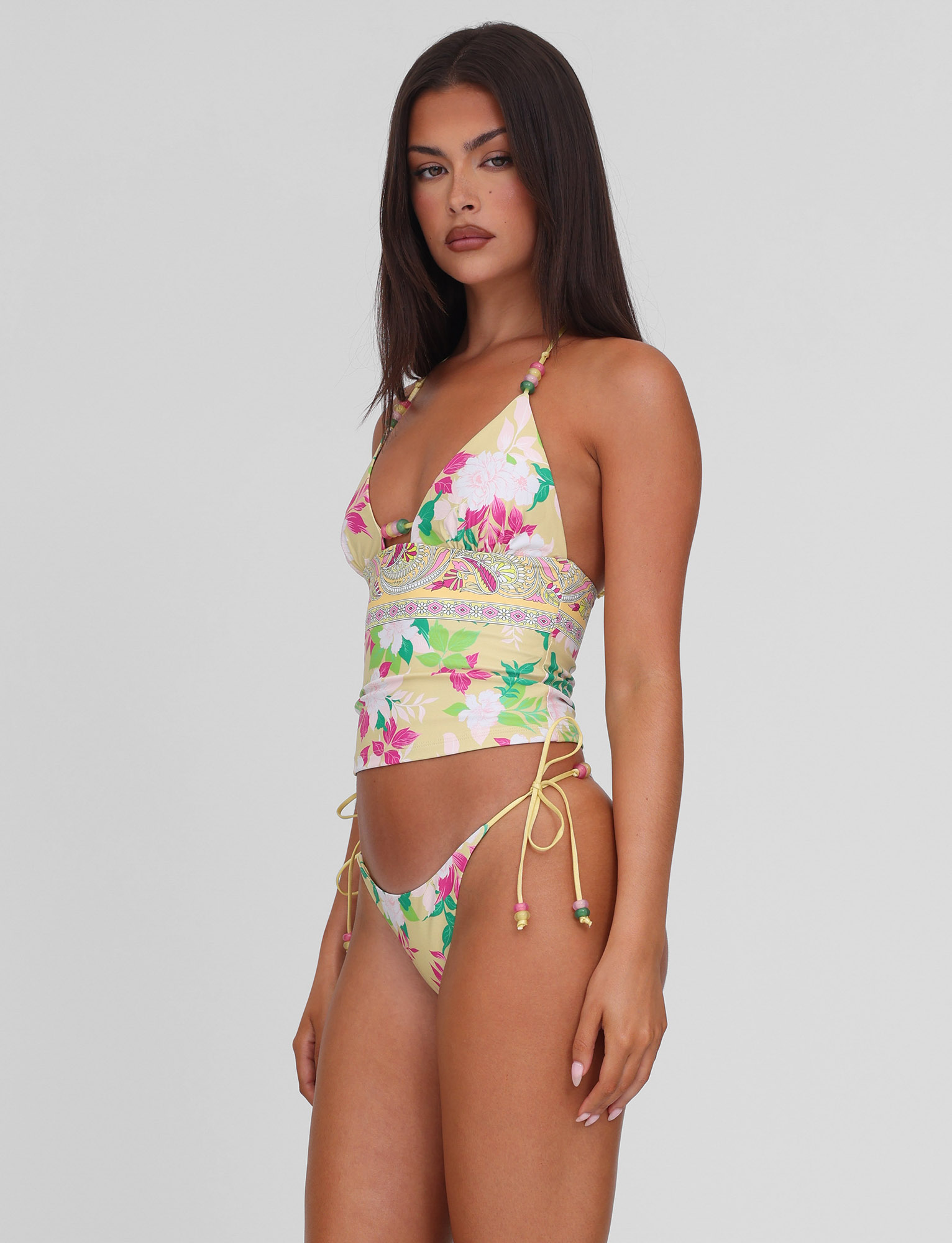 A woman wears the TIGERMIST FINLEA TANKINI TOP - PAISLEY BORDER, a floral and paisley print swimsuit, standing confidently against a light gray background.