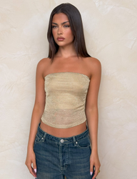 A woman with straight brown hair wears the TIGERMIST HARRIETT TUBE TOP in gold and blue jeans, standing against a light textured wall with a neutral expression.