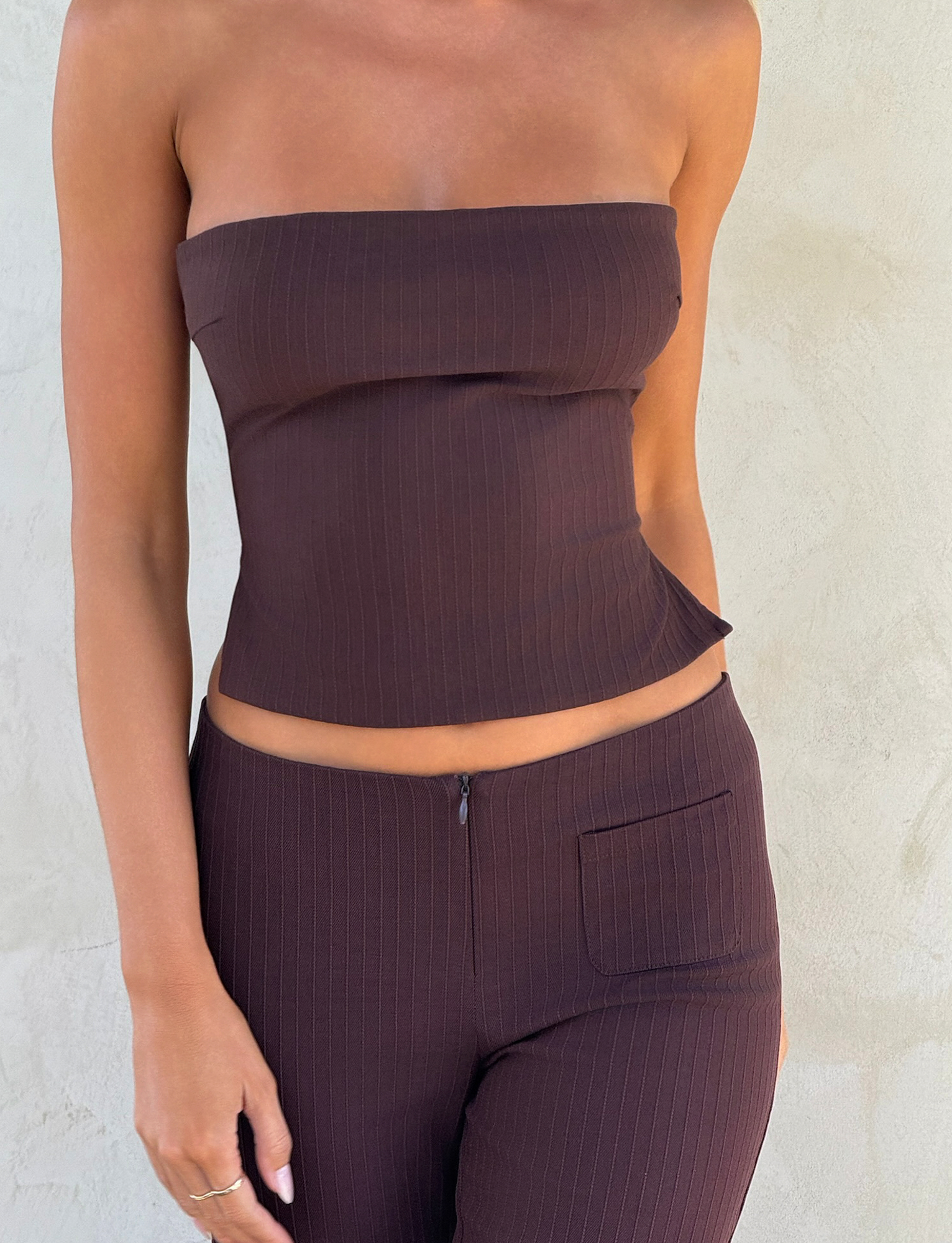 A person wears the TIGERMIST GWENDOLINE TOP in chocolate with matching high-waisted, subtly striped pants, standing against a light textured wall—only their torso and upper legs are visible.