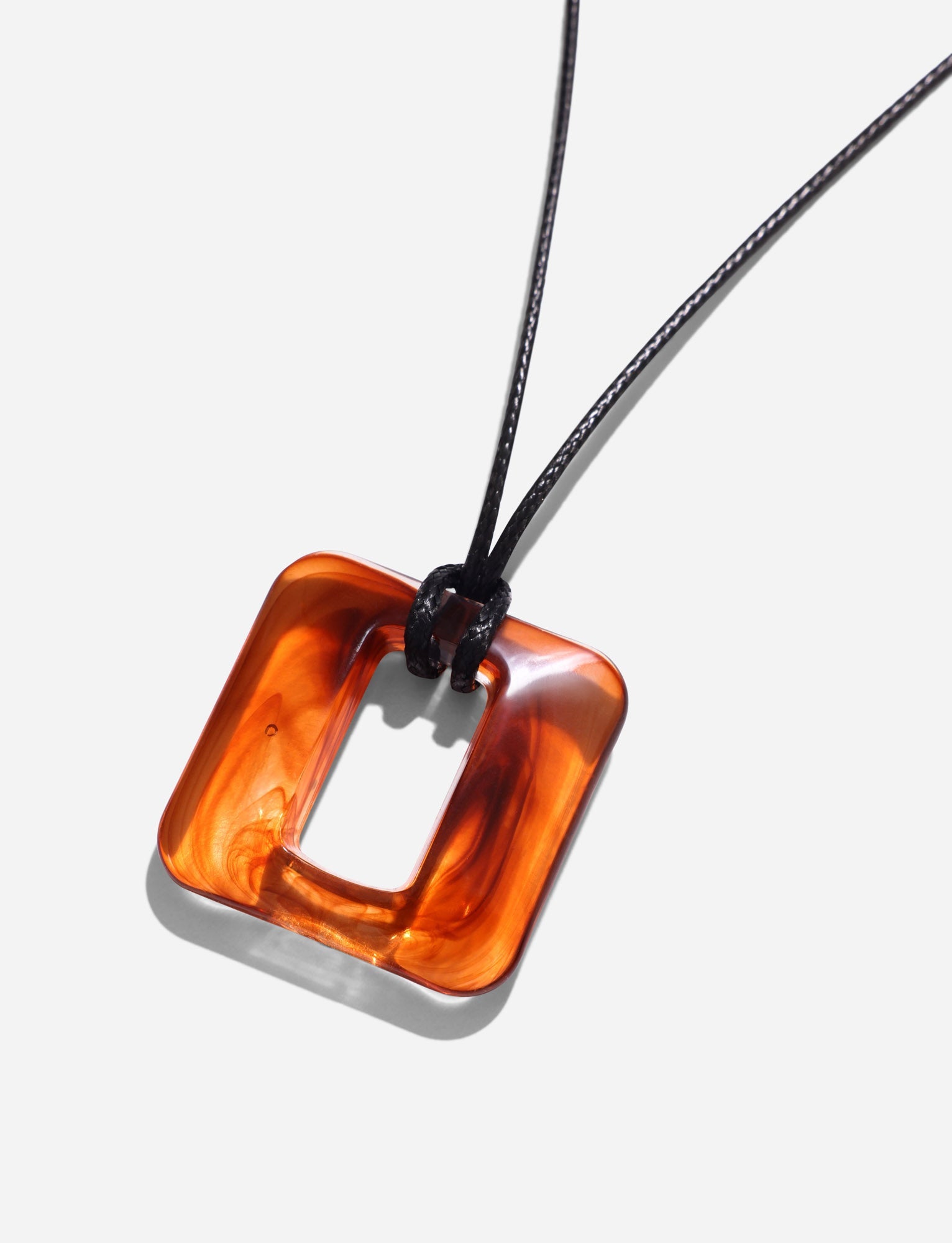 TIGERMIST's MIRREN SQUARE NECKLACE in brown features a marbled amber square pendant with a central cutout. It hangs from an adjustable black cord and is crafted from resin.