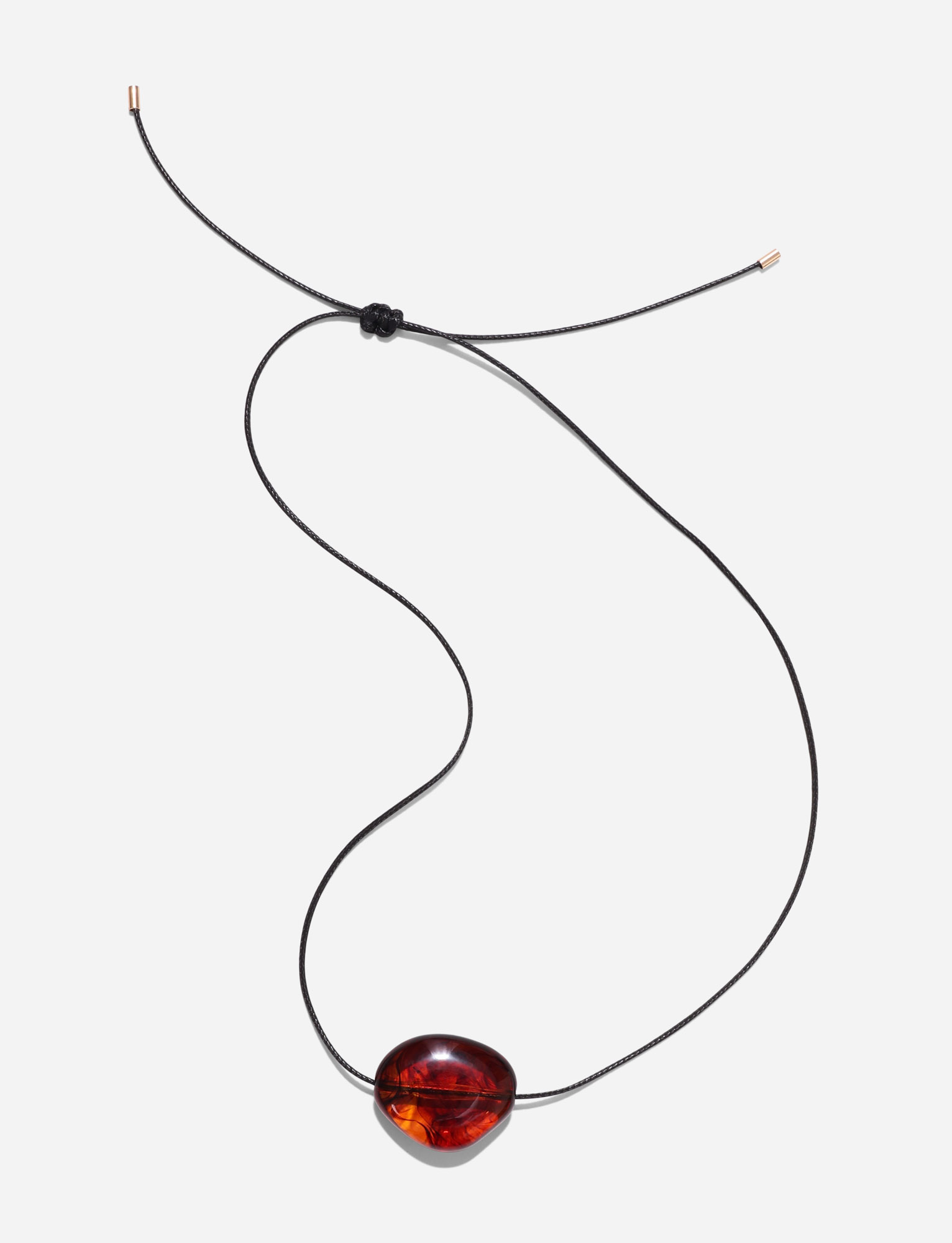 The SOLENE NECKLACE - BROWN by TIGERMIST features a minimalist black cord with an adjustable knot and a polished, oval amber pendant. It is shown laid flat on a white background.