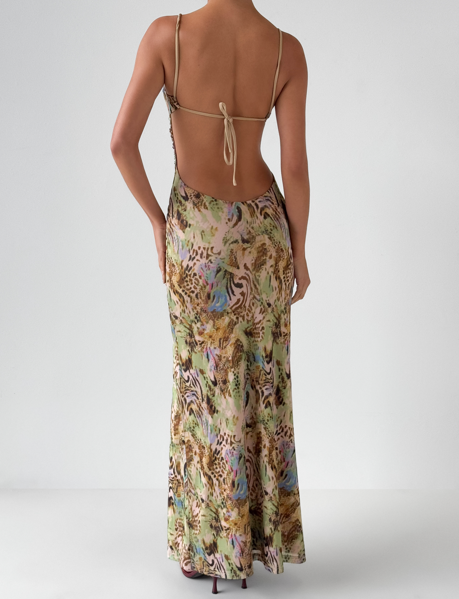 A person stands facing away against a plain white background, wearing the TIGERMIST ELYSIUM MAXI DRESS - ANIMAL SWIRL, a yellow animal print maxi dress with thin straps and a sequin neckline.