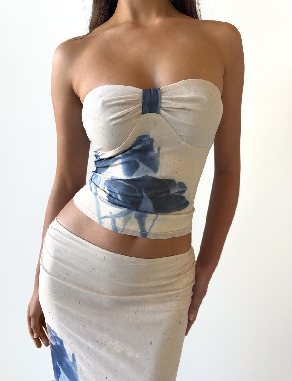 A woman wears the JANIS TOP - INDIGO FLORAL by TIGERMIST, a strapless sweetheart tube top with blue floral print mesh, standing against a plain white background.