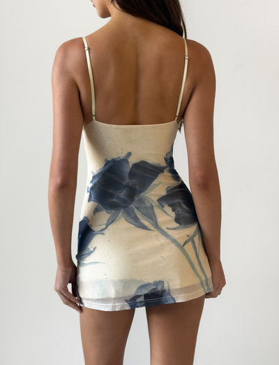 A woman models the TIGERMIST ROSY MINI DRESS - INDIGO FLORAL with adjustable cami straps, standing with her back to the camera against a white background.