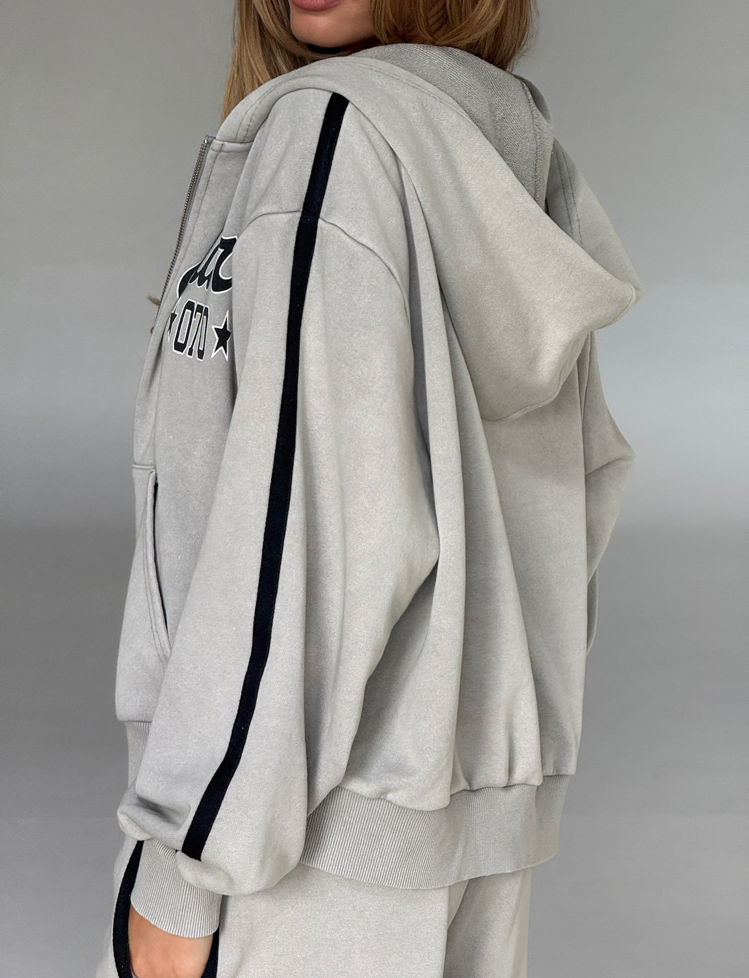 A person wearing the TIGERMIST PAYTON HOODIE in stone gray with black striped sleeves and matching pants stands sideways against a neutral background.