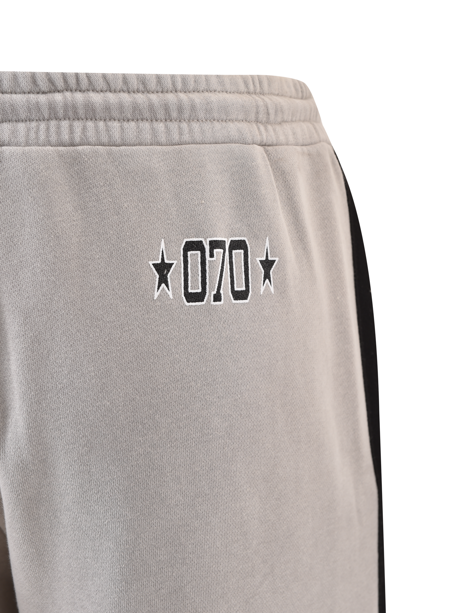 Close-up of TIGERMIST PAYTON TRACKPANT - STONE: grey trackpants with black "070" outline and star accents near the pocket, plus a sporty black side stripe.