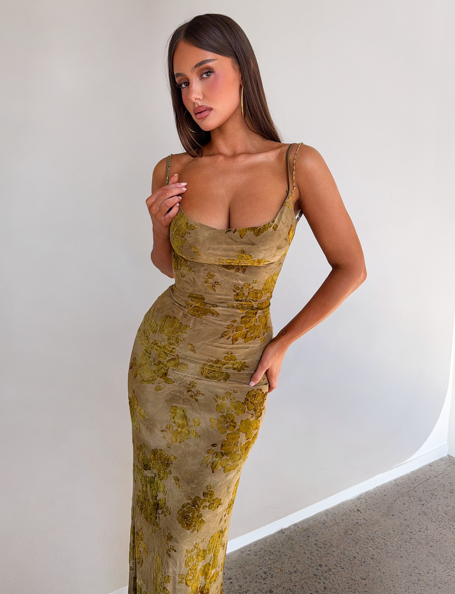 A woman with long brown hair poses confidently in the TIGERMIST SPARROW MAXI DRESS - GREEN BURNOUT against a plain light background, standing with one hand on her hip and the other touching her dress strap.