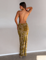 A woman faces away, wearing the TIGERMIST SPARROW MAXI DRESS in green burnout with gold chain straps and large hoop earrings, standing against a plain light-colored wall.