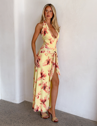 A woman poses indoors in the TIGERMIST ALLEGRA MAXI DRESS in yellow watercolour floral, featuring a sleeveless design, deep V-neckline and high leg split. She has long blonde hair and pairs the look with chic heeled sandals.