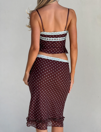 A woman with long blonde hair, seen from behind, wears the TIGERMIST AMARA MIDI SKIRT - POLKA DOT and a matching spaghetti-strap top, standing against a plain light background.