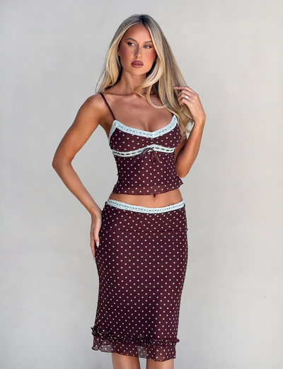 A woman with long blonde hair wears the TIGERMIST AMARA MIDI SKIRT - POLKA DOT, a brown two-piece outfit with light blue lace trim and a fitted camisole, posing against a plain light background.