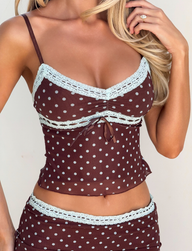 A woman wears the TIGERMIST AMARA TOP - POLKA DOT, a brown cami with white lace trim and matching bottoms. Her long blonde hair falls loosely as she holds a strand with her left hand.