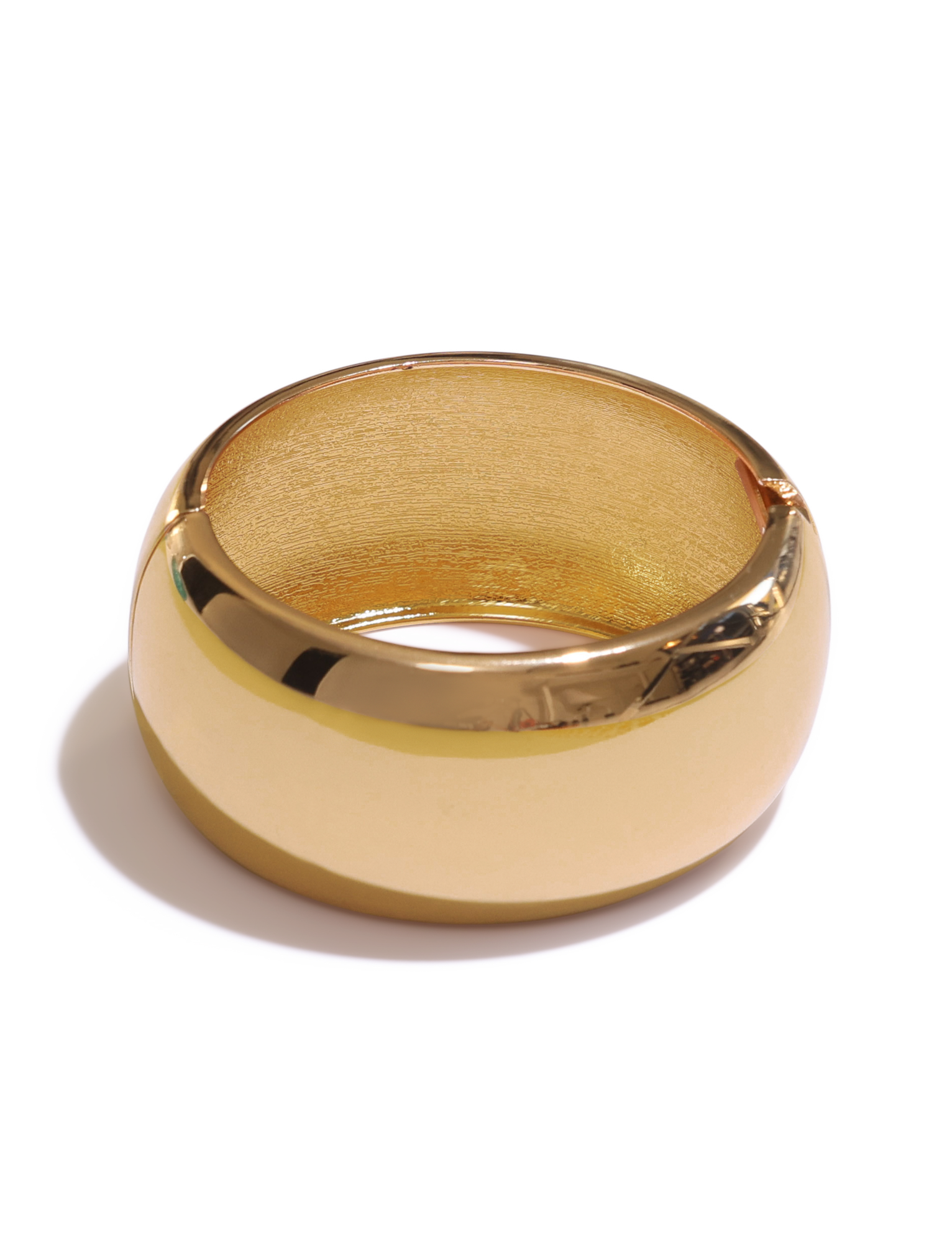 The MIRAH CHUNKY BANGLE - GOLD by TIGERMIST is shown against a white background, its wide, polished gold surface casting a soft shadow and evoking the look of a sleek gold cuff bracelet.