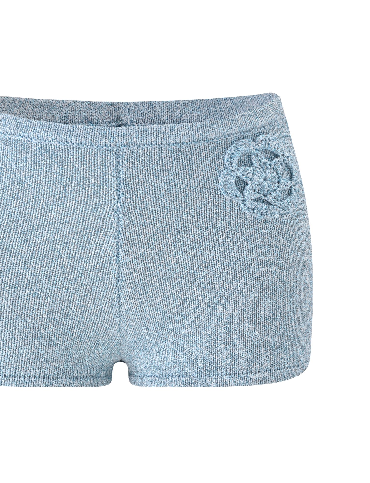The SUNIA SHORT - BLUE by TIGERMIST are light blue ultra-mini hot shorts with a crocheted flower appliqué on the left hip and a soft, textured fabric. Only the lower torso and upper thigh area are shown.