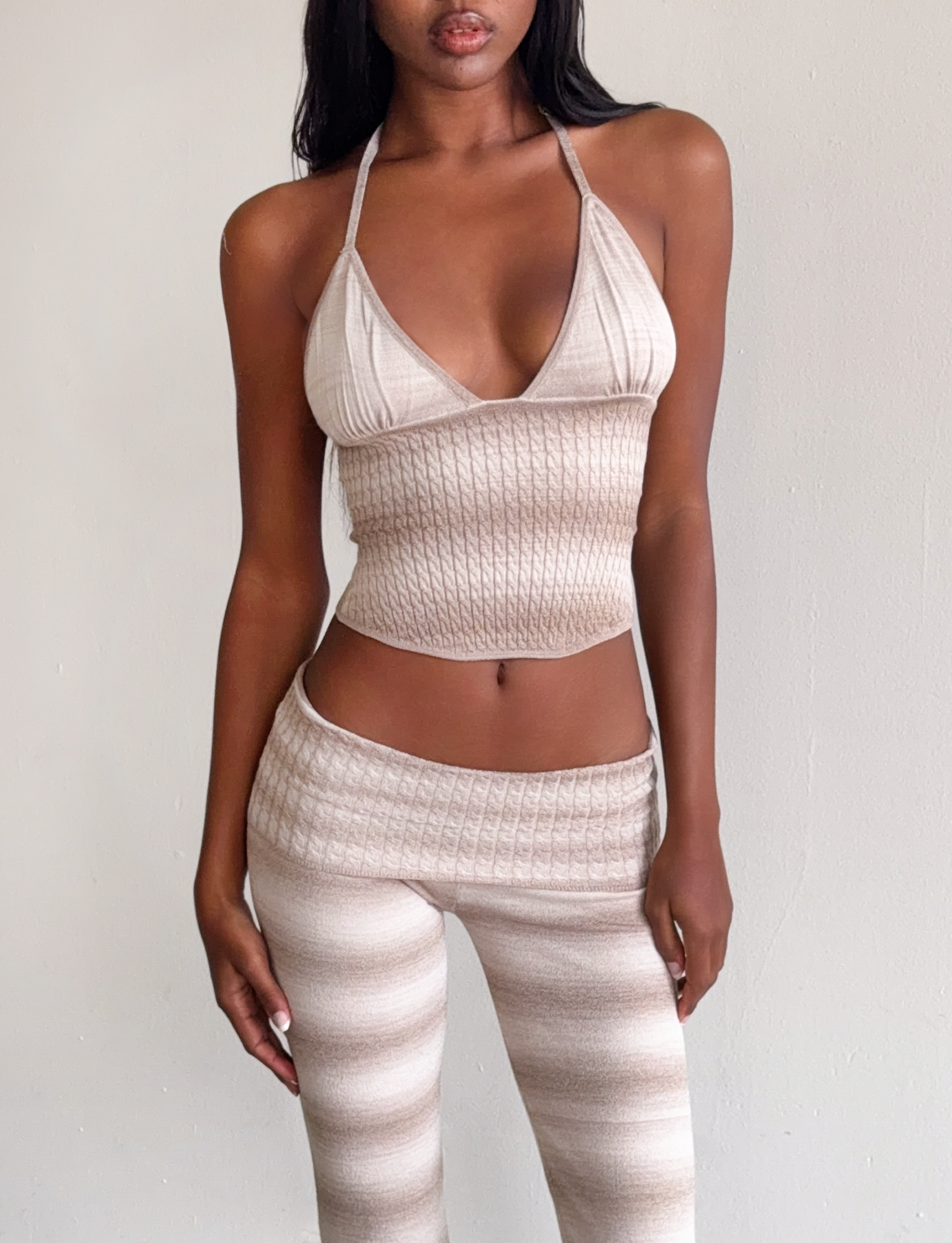 A woman wears the TIGERMIST MARISSA KNIT CAMI in taupe ombre stripe with matching high-waisted pants, standing against a plain light-colored wall.