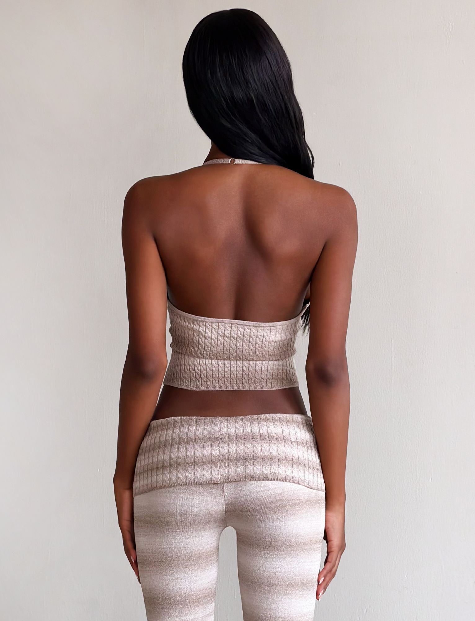 A woman with long dark hair stands with her back to the camera, wearing the TIGERMIST MARISSA KNIT CAMI in taupe ombre stripe and matching high-waisted pants against a plain light background.