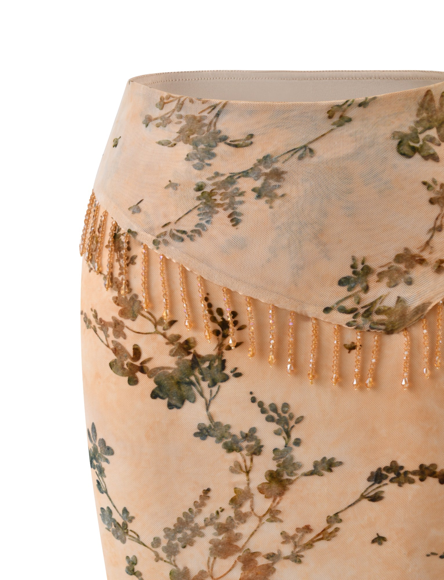A close-up of the TIGERMIST OONA BURN OUT FRINGE SKIRT in tan, showcasing a beige floral midi design with a sheer overlay and removable waistband adorned with dangling beaded fringe, set against a plain white background.
