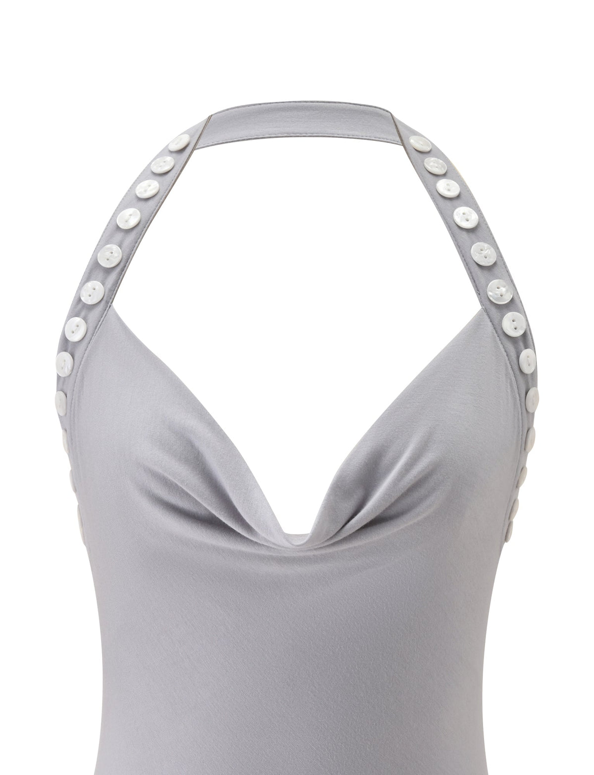 The image features the SUKI TOP - GREY by TIGERMIST, a light gray halter-neck top designed with a draped cowl neckline and distinctive white buttons adorning both halter straps. Crafted from soft, slightly stretchy fabric, this top combines comfort and style. Only the upper portion of the garment is visible against a plain background.