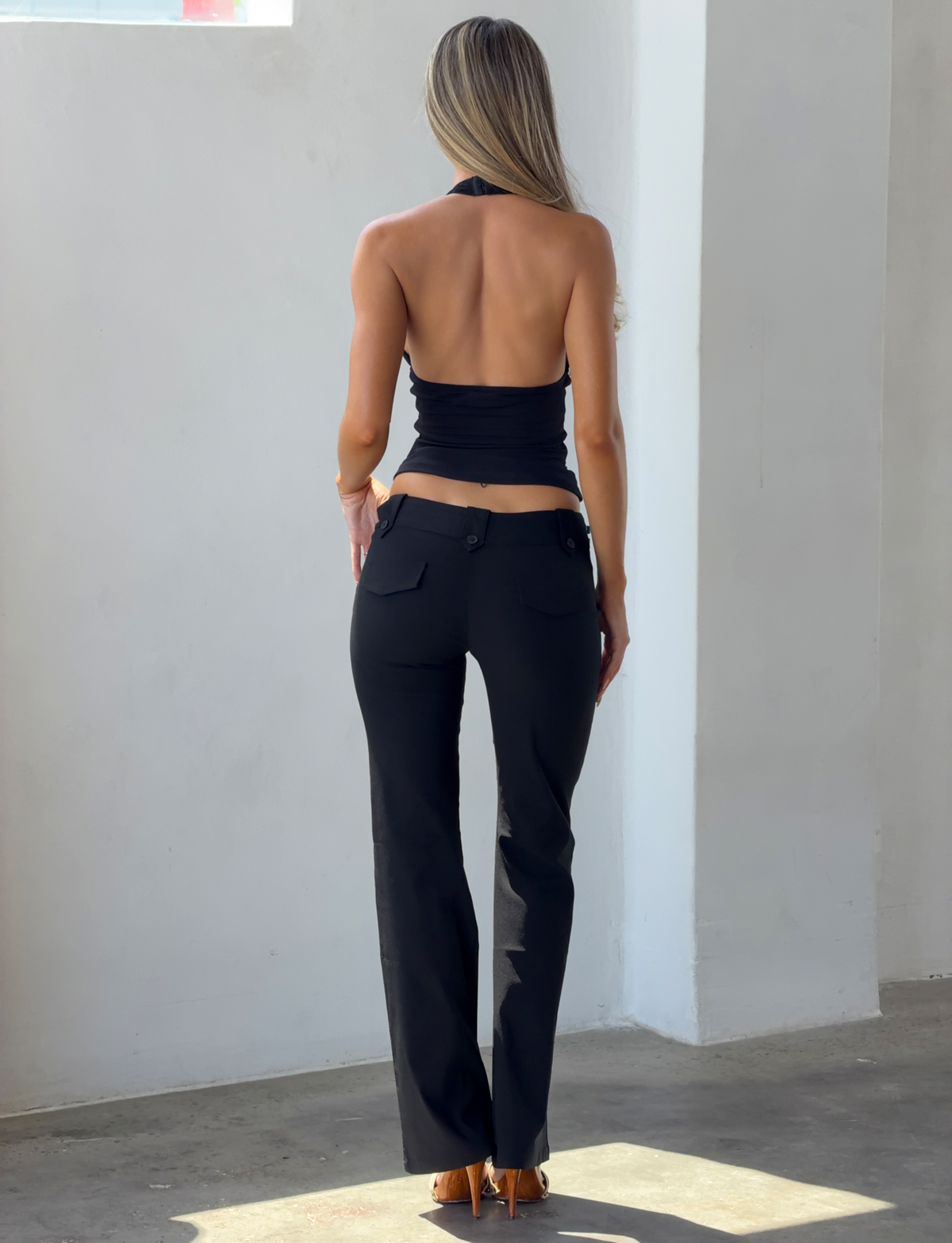 A person seen from behind wearing a black mesh NINAH TOP - BLACK halter top and black trousers.