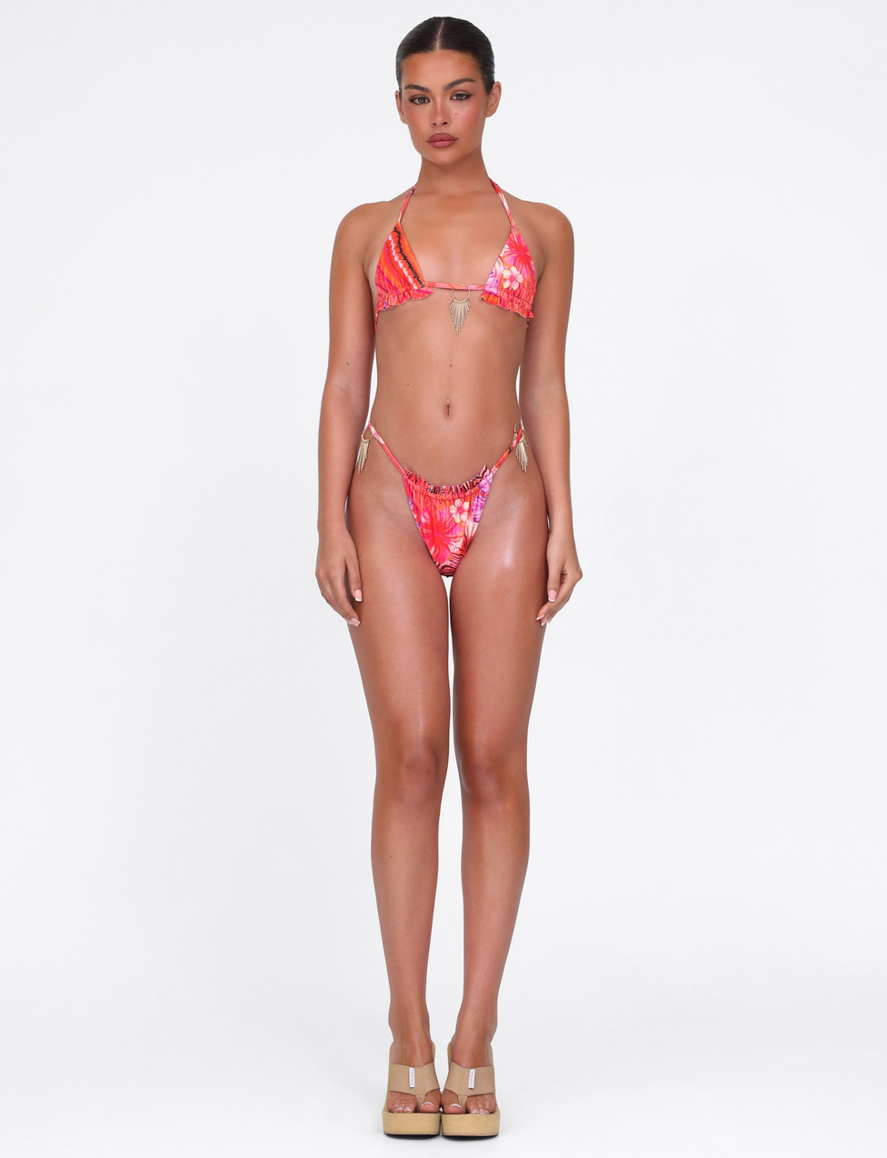 A woman faces forward against a plain white background, wearing the TIGERMIST CIANA BIKINI TOP in Pink Tropical Floral and beige platform heels.