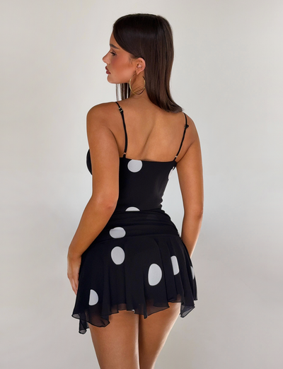 A woman with straight brown hair is wearing the TIGERMIST AYDIN SCARF TOP in black. She stands against a plain light background, facing away and looking to the side.