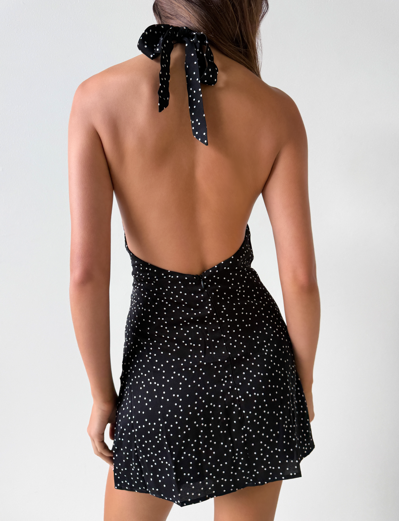 A woman with long brown hair, seen from behind, models the Third Party DYLAN HALTER MINI DRESS - BLACK POLKA with a low-cut back against a plain light background.
