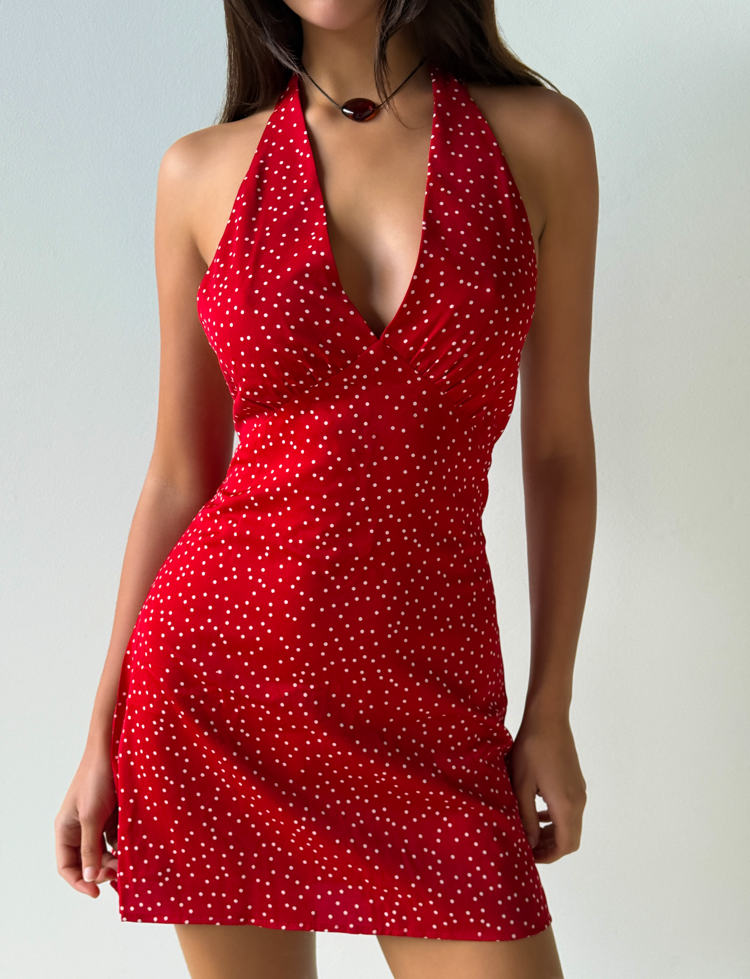 A woman wears the Tiger Mist USA CL - DYLAN HALTER MINI DRESS, a sleeveless red halter-neck mini dress with white polka dots, standing against a plain light background.