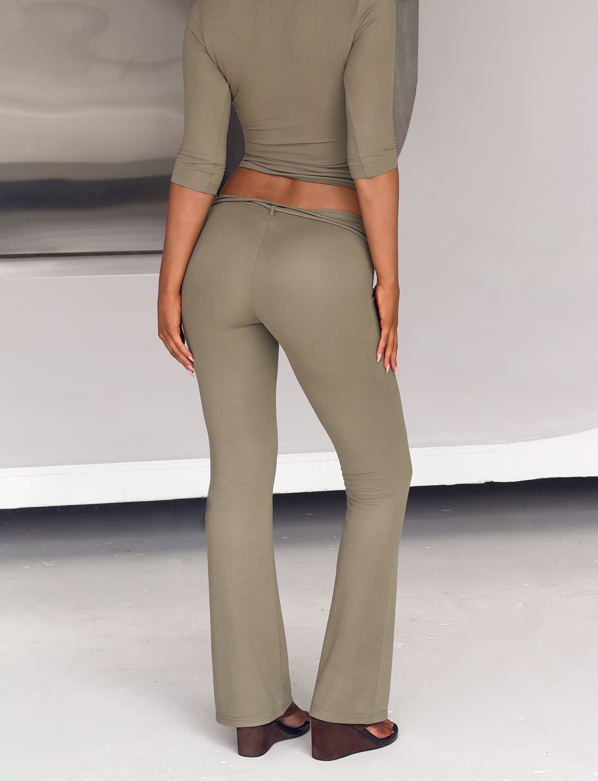 Back view of a person wearing the olive green KHORA PANT - OLIVE, a matching cropped top, and dark wedge sandals.