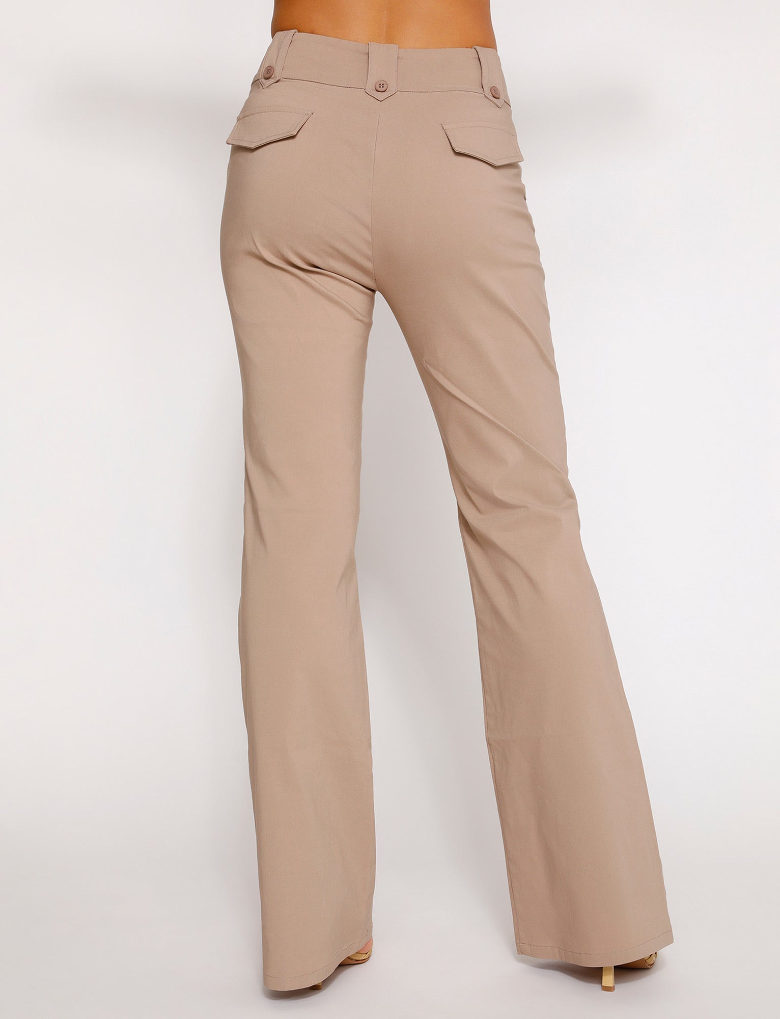 A person wearing the TIGERMIST Kittie High Rise Pant in beige (tan) is shown from the back. The high-waisted, flared trousers feature flap pockets with buttons on the rear and slight creases down the legs. The background is plain white.