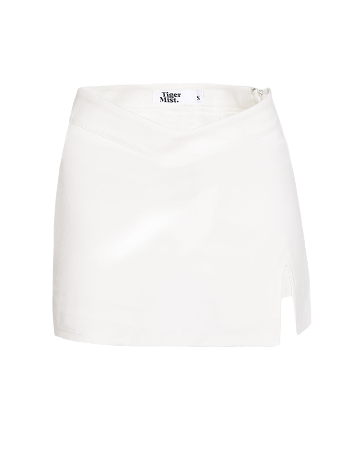 The DAPHNIE PU SKORT in white, from TIGERMIST, features a high-waisted design with a subtle drape effect at the waistband and a small slit on the left side. The tag inside reads "TIGERMIST" and indicates the size as small (S). The fabric is smooth and slightly reflective, capturing TIGERMIST's signature sleek aesthetic.