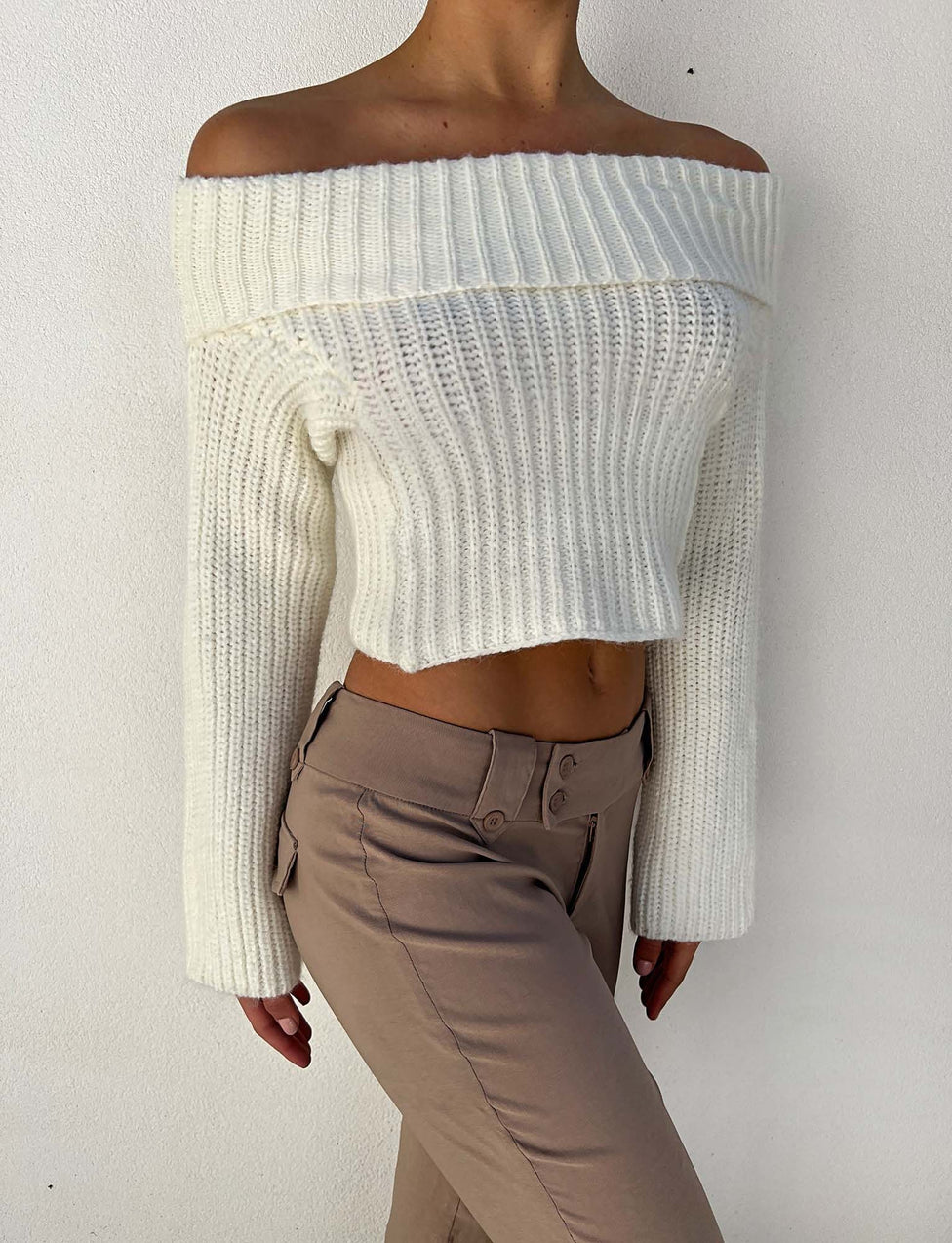 A person is wearing the ASHLYN JUMPER - WHITE from TIGERMIST, paired with beige high-waisted pants. The outfit accentuates the midriff and exudes a casual, stylish vibe. The photo is taken against a plain white background.