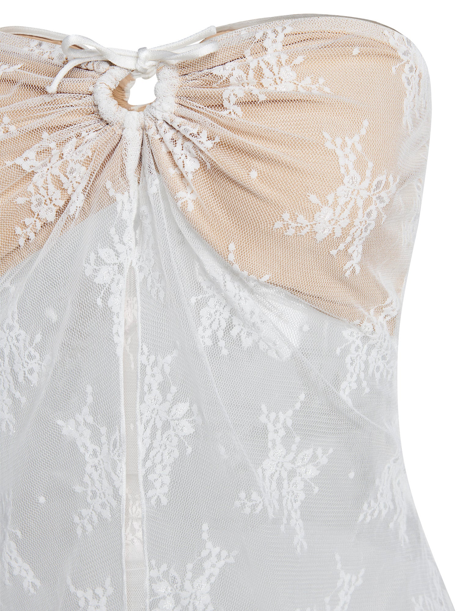 A close-up image of the KAROLINA TOP by TIGERMIST features intricate white lace material with floral patterns on a nude underlay. The top includes gathered detail at the center bust, held by a white string tied in a bow, with the lace design continuing throughout the fabric.