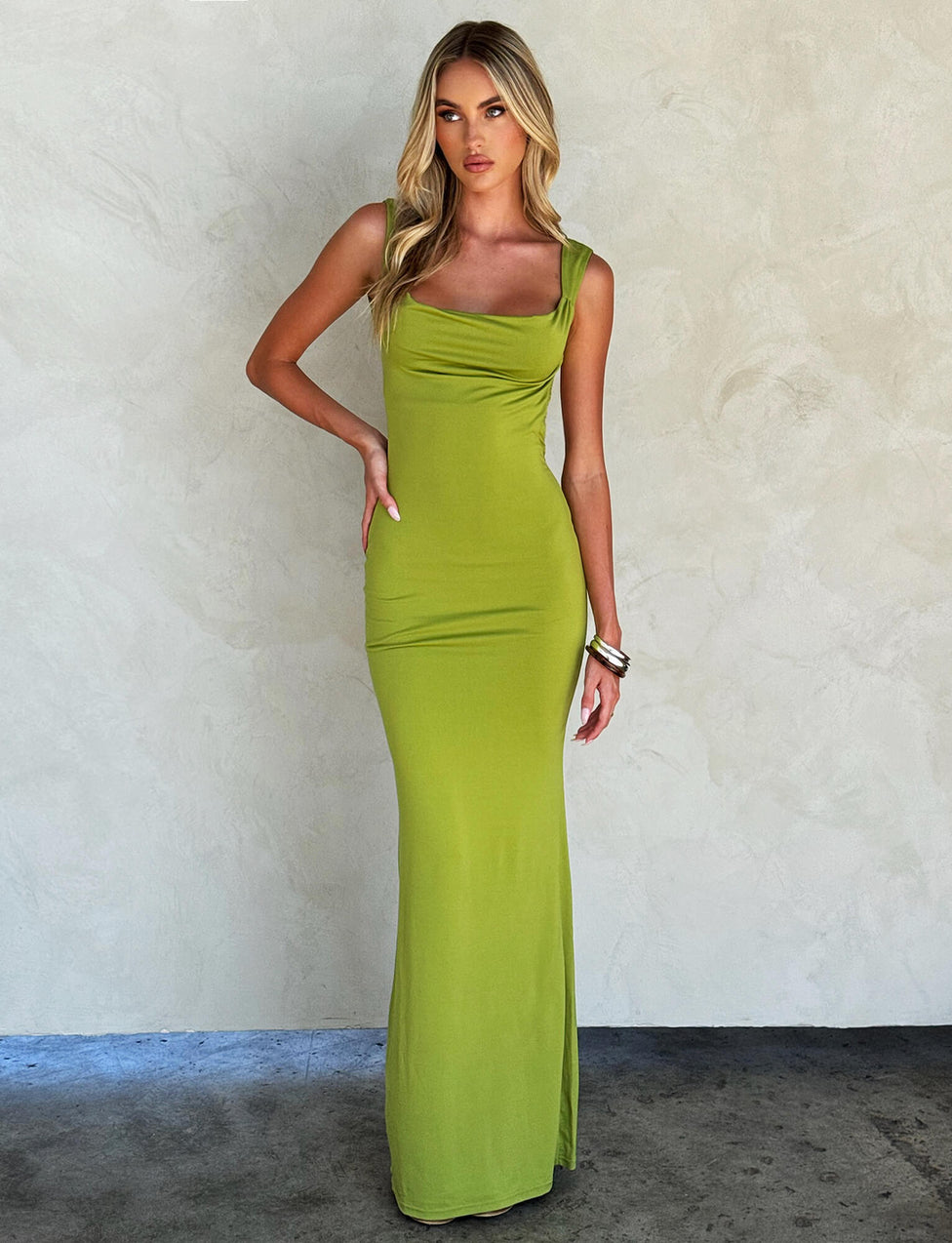 A person with long blonde hair is wearing the form-fitting, sleeveless MORANA DRESS - GREEN : PASTEL GREEN from TIGERMIST, featuring a square neckline. They are standing against a neutral textured background, with one hand on their hip and the other relaxed by their side.